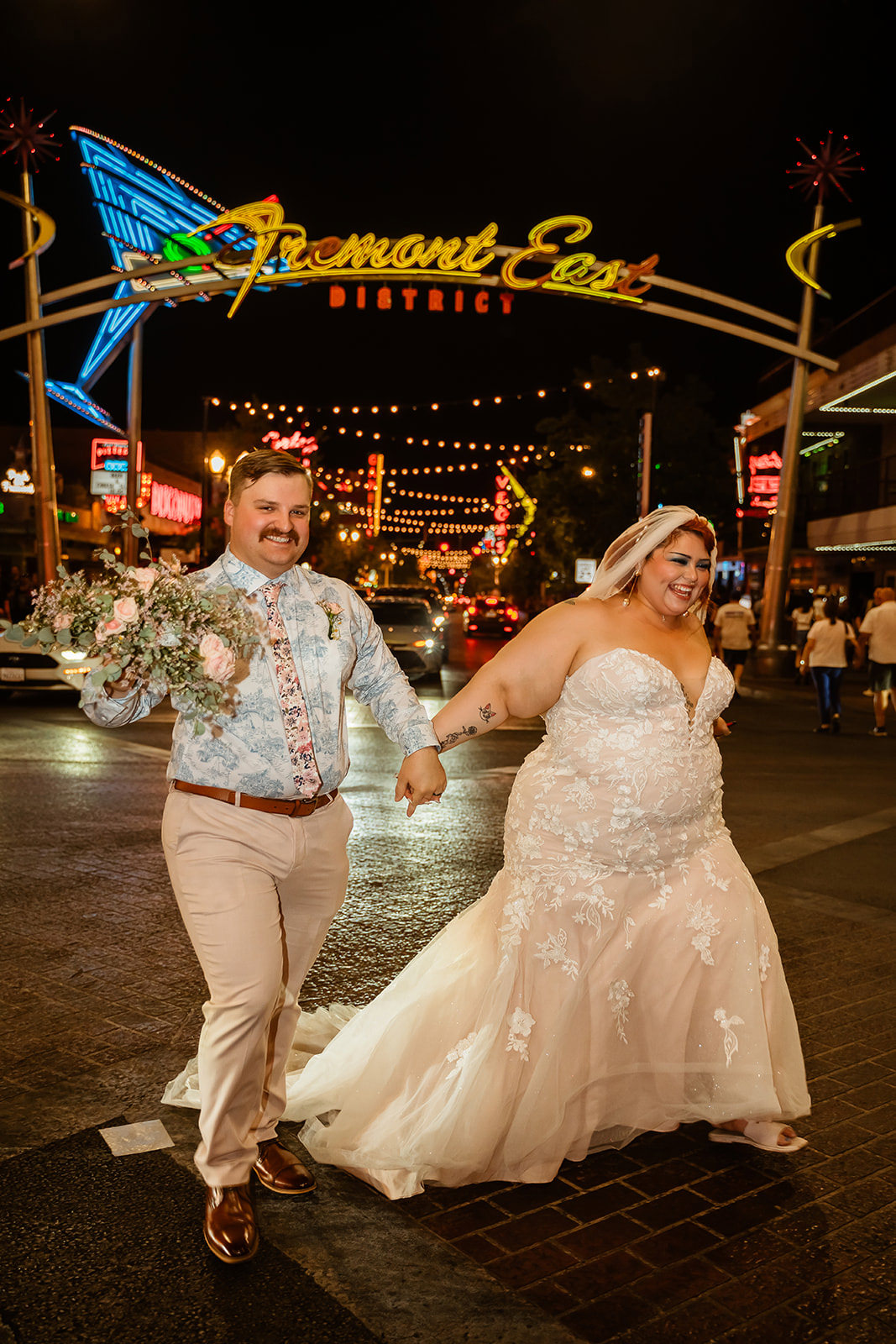 Las Vegas elopement couple walking under Fremont East District sign on Fremont Street at night