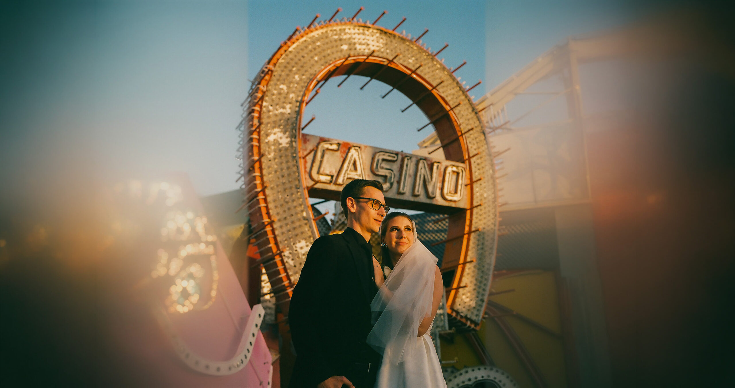 Bride and groom posing under vintage casino sign at Las Vegas Neon Museum during golden hour sunset